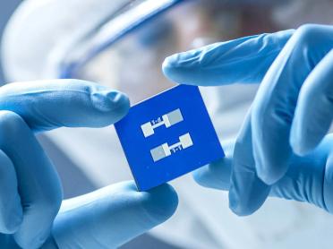 A chip is held between two gloved hands.