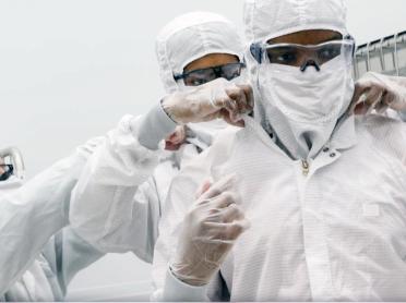 Three students gown up in bunny suits before entering MIT.nano's cleanroom.