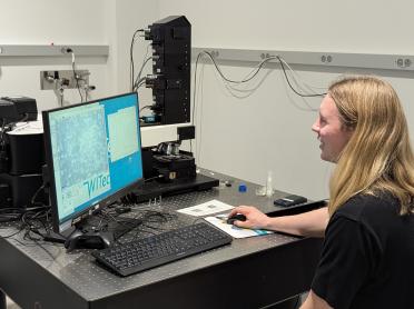 A person sits at a computer that is displaying data from a microscope.